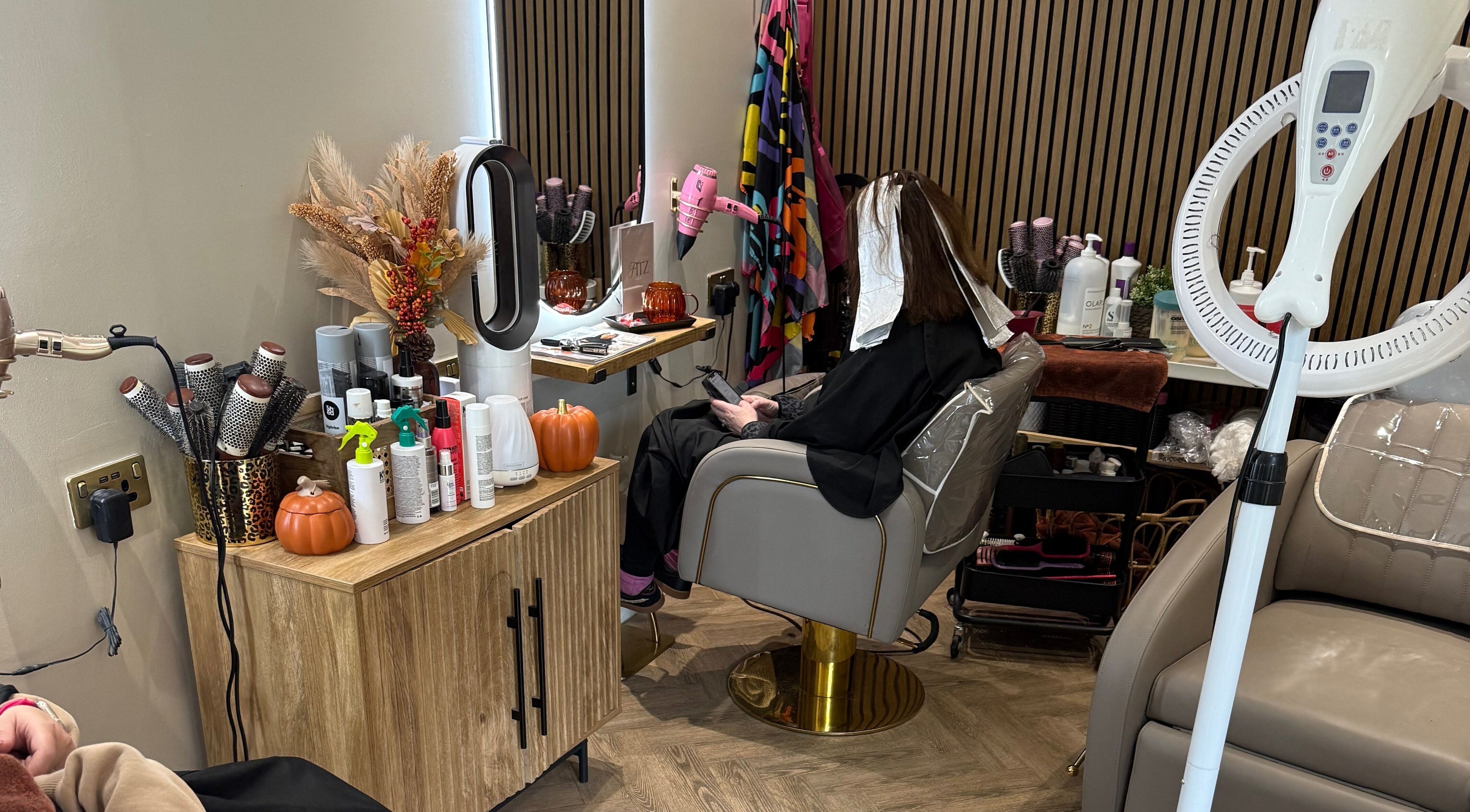 Client in styling chair at Kate Fitzpatrick Hair, Deeside, Wales, GB, surrounded by beauty products.