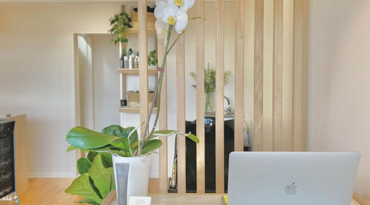 Reception area of Muse Hair Studio in Bay of Plenty, NZ with laptop and orchid decor.