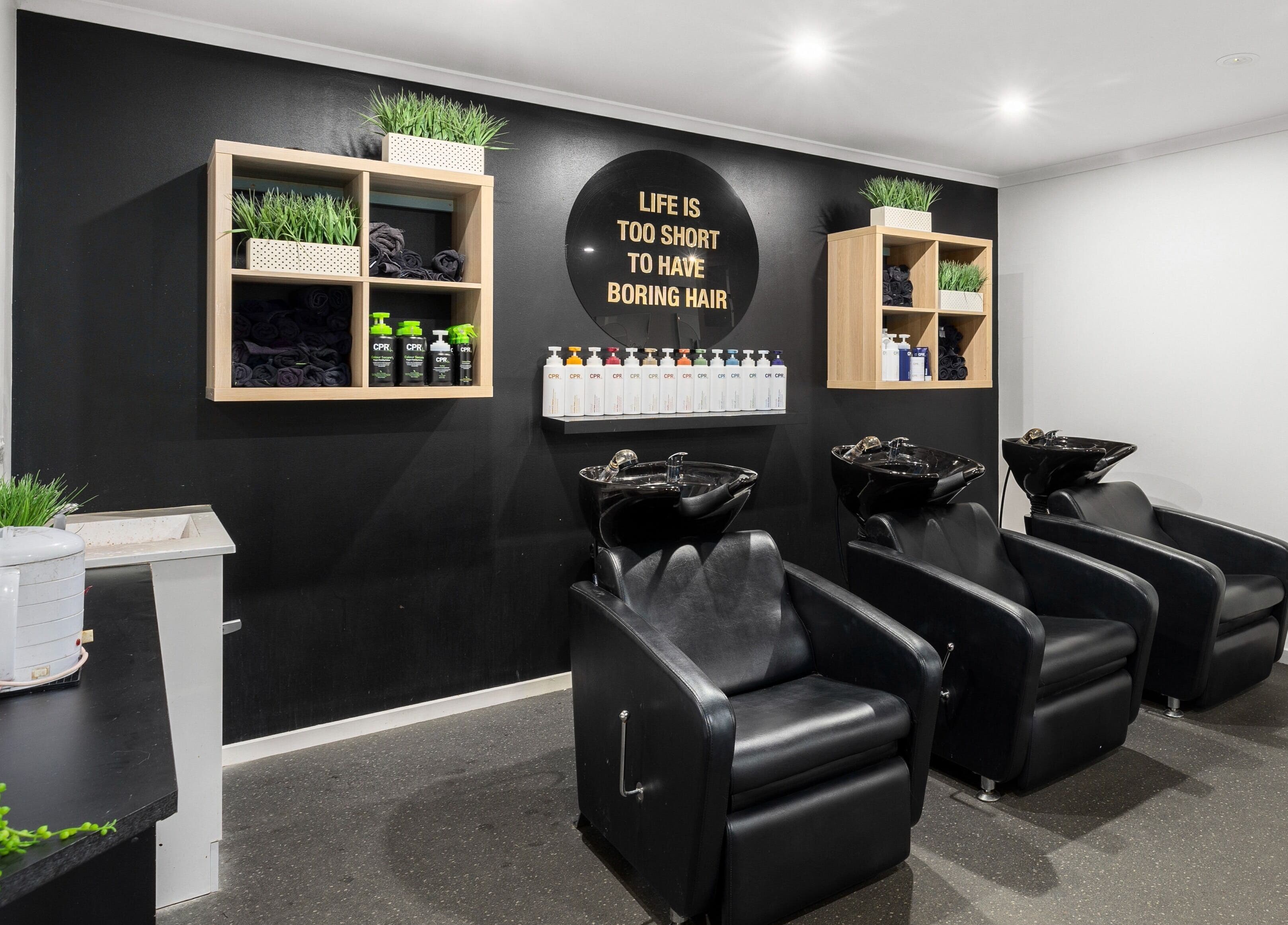 Modern hair washing station at Mane Studioz, Bongaree, Queensland, AU, featuring sleek black chairs and shelving.