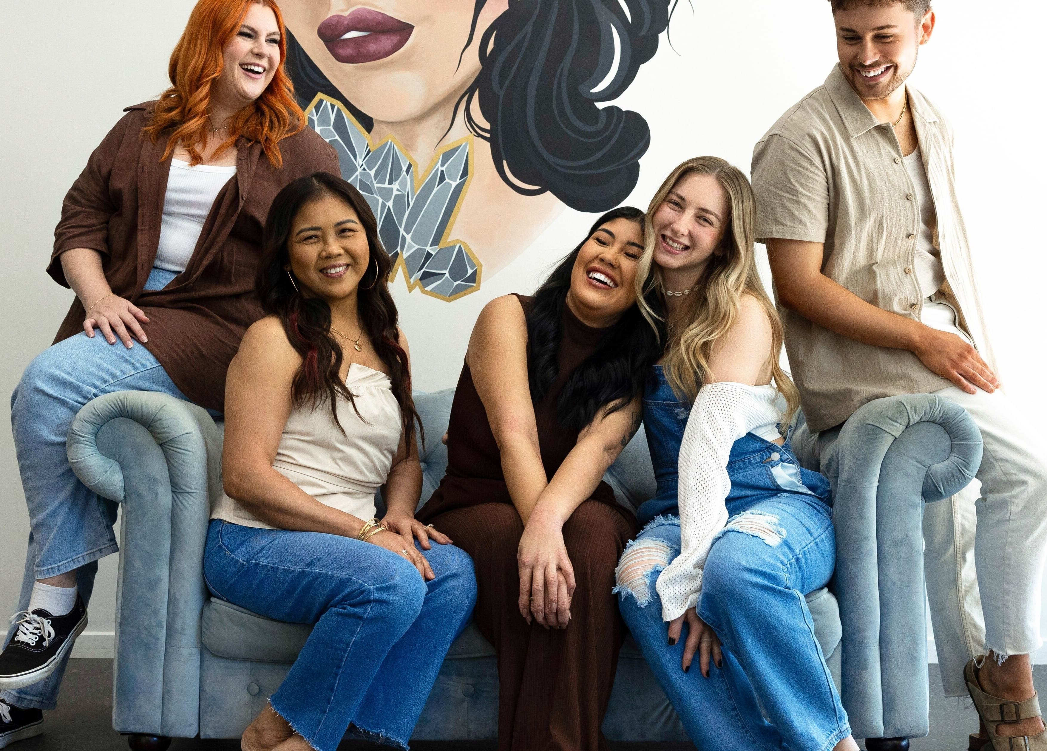 Smiling team at Mane Studioz in Bongaree, Queensland, AU, sitting on a stylish couch with vibrant wall art.