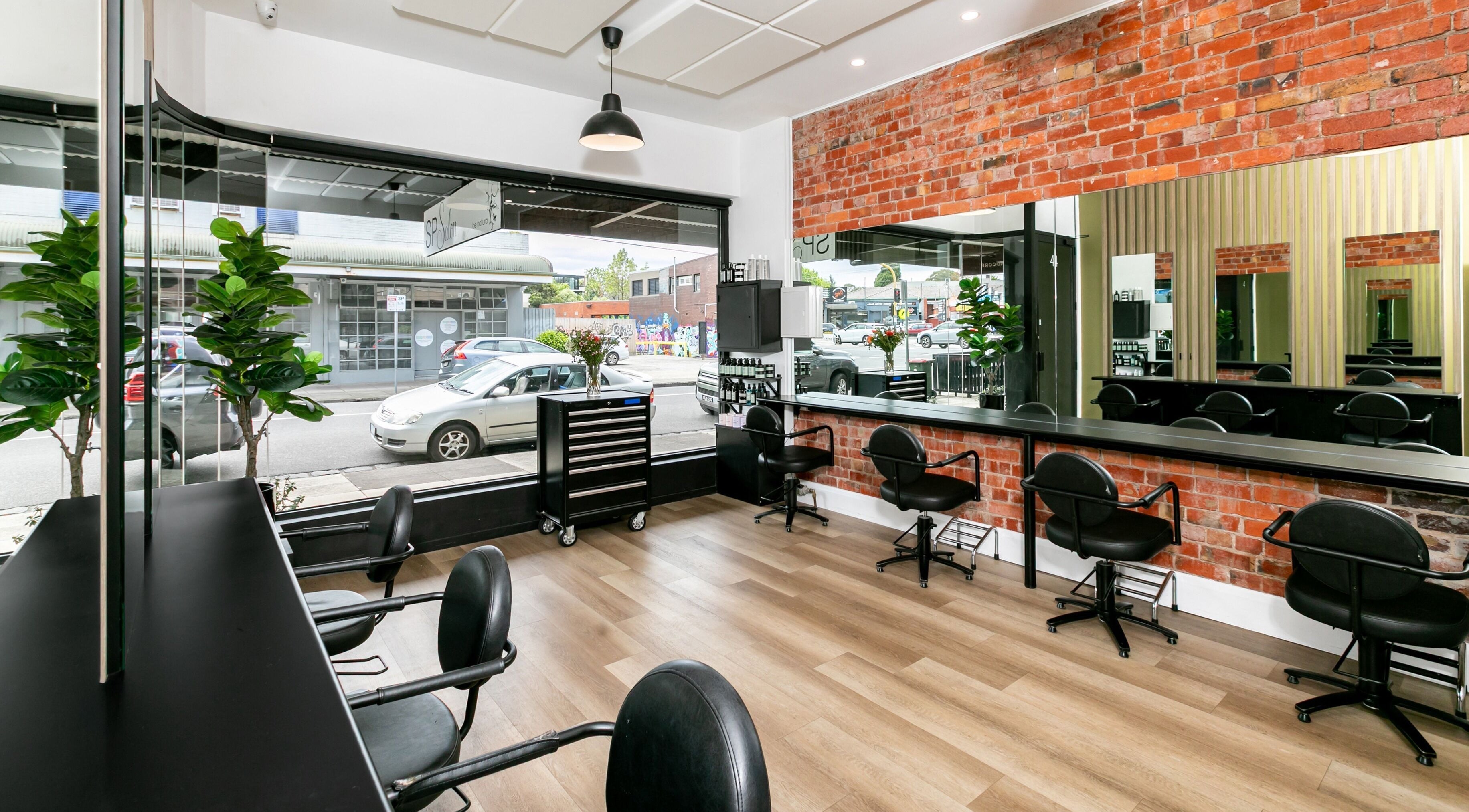 Modern interior of SP Salon in Melbourne, Victoria, AU, featuring sleek black chairs and brick accents.