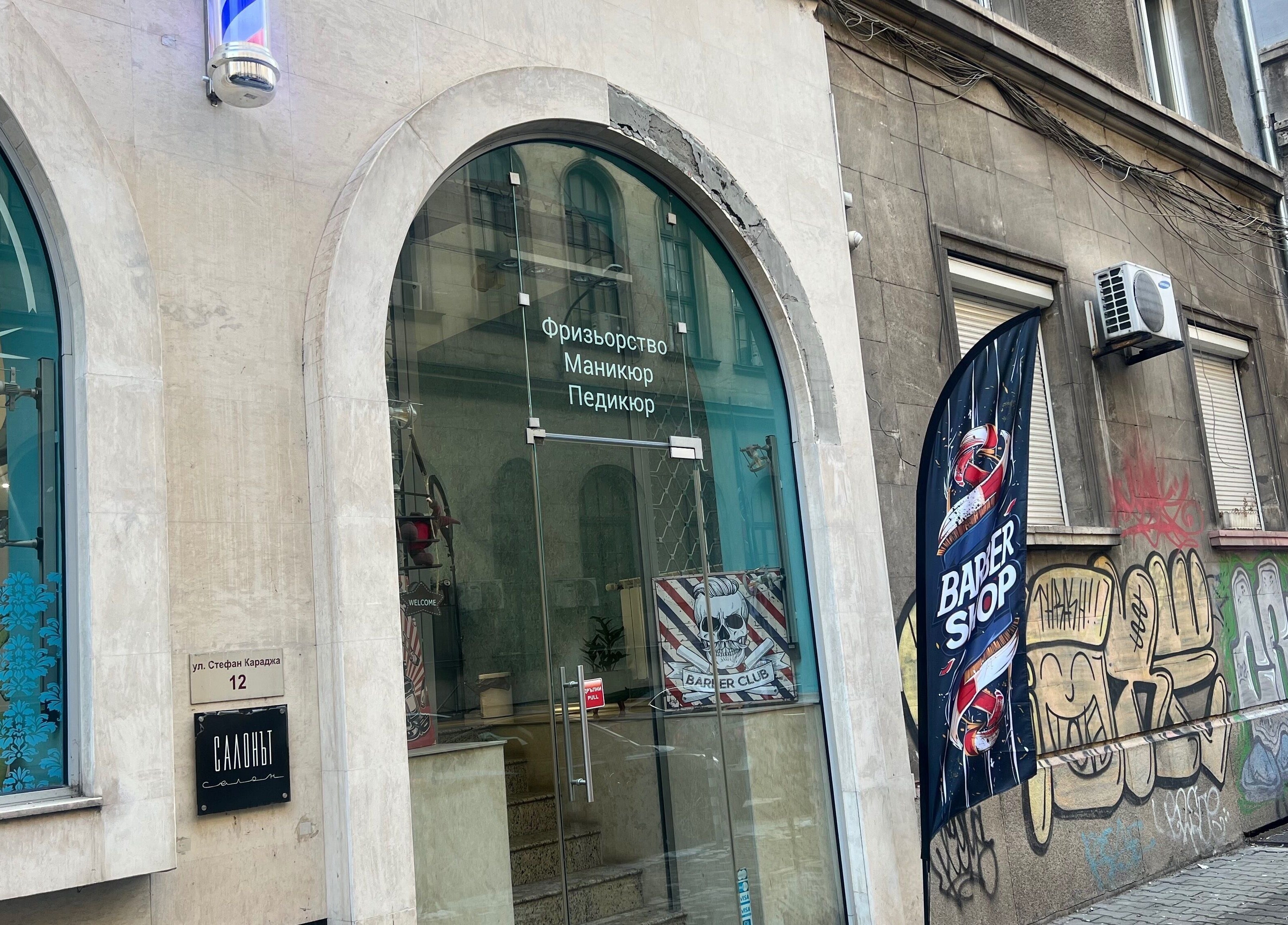 Входът на The Barbershop Mudi в София, Софийска област, BG с модерни стъклени врати и голяма витрина.