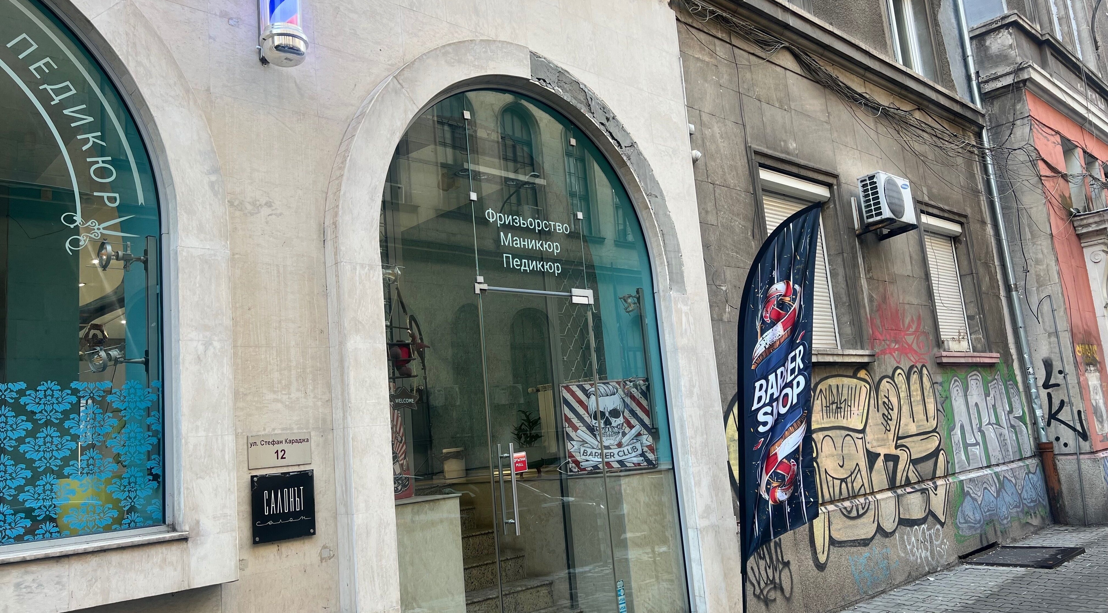 Входът на The Barbershop Mudi в София, Софийска област, BG с модерни стъклени врати и голяма витрина.