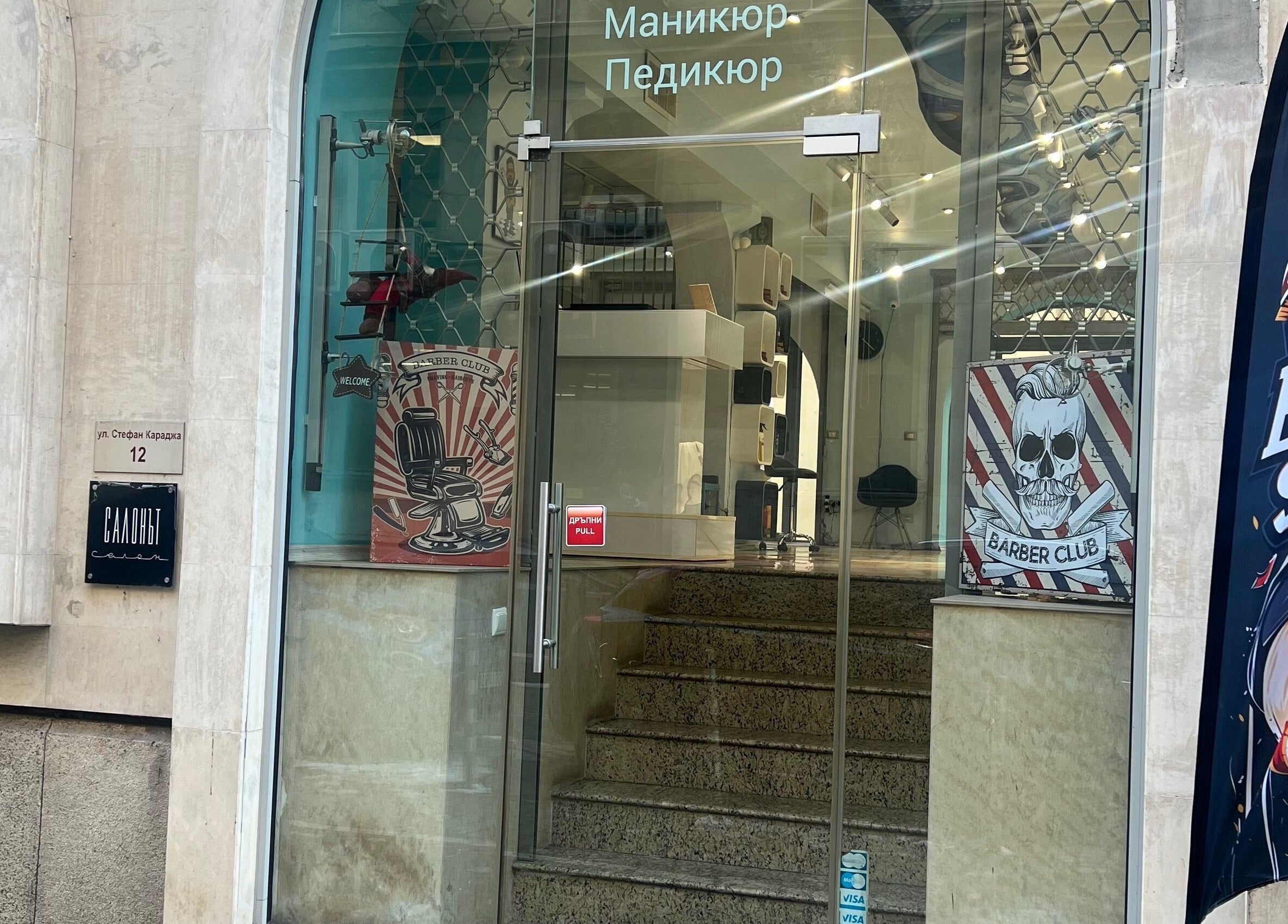Вход на The Barbershop Mudi в София, София град, BG с модерна стъклена врата и барбер декорации.
