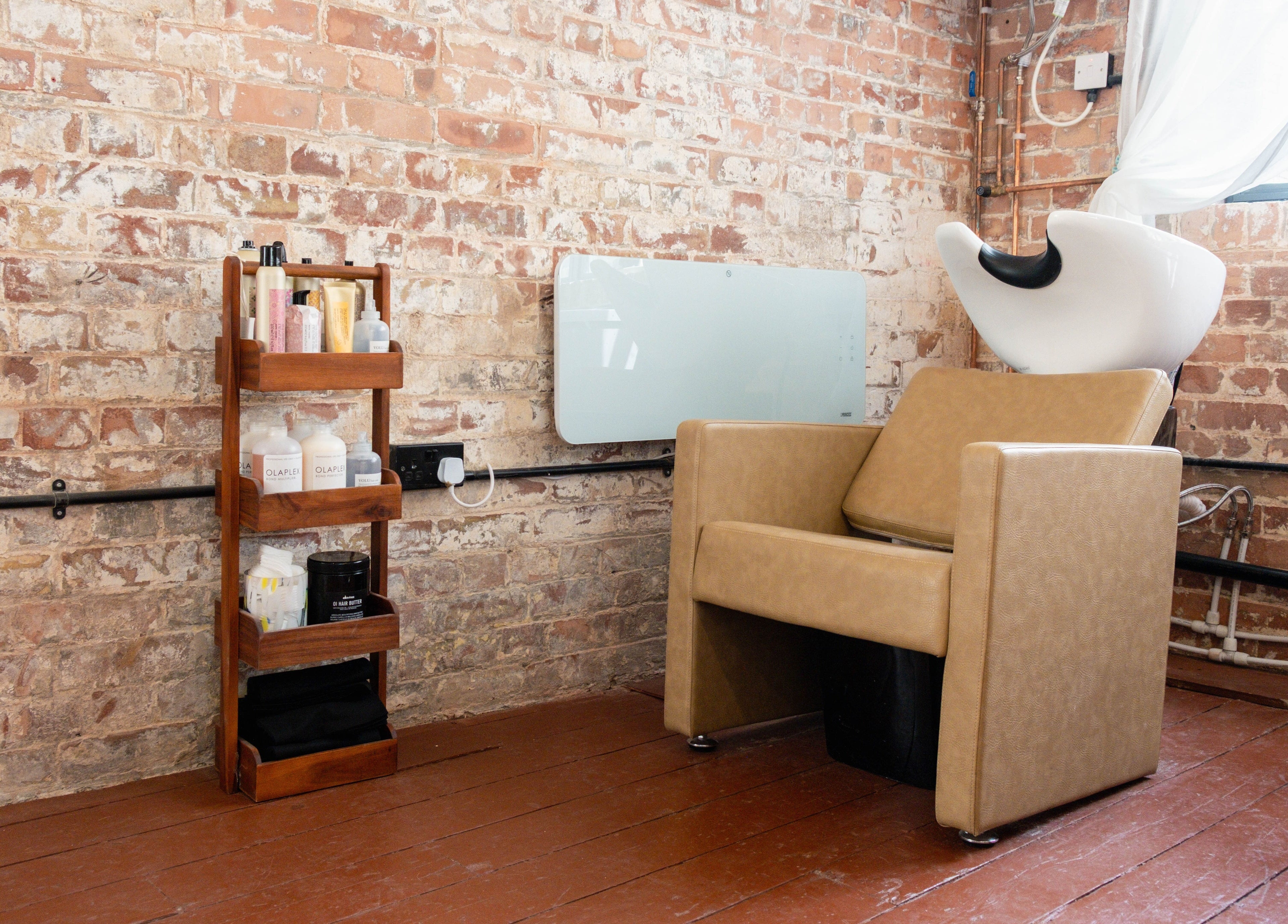 Cozy salon corner at Fluff.Hackney, London, England with a shampoo chair and product shelf against brick wall.
