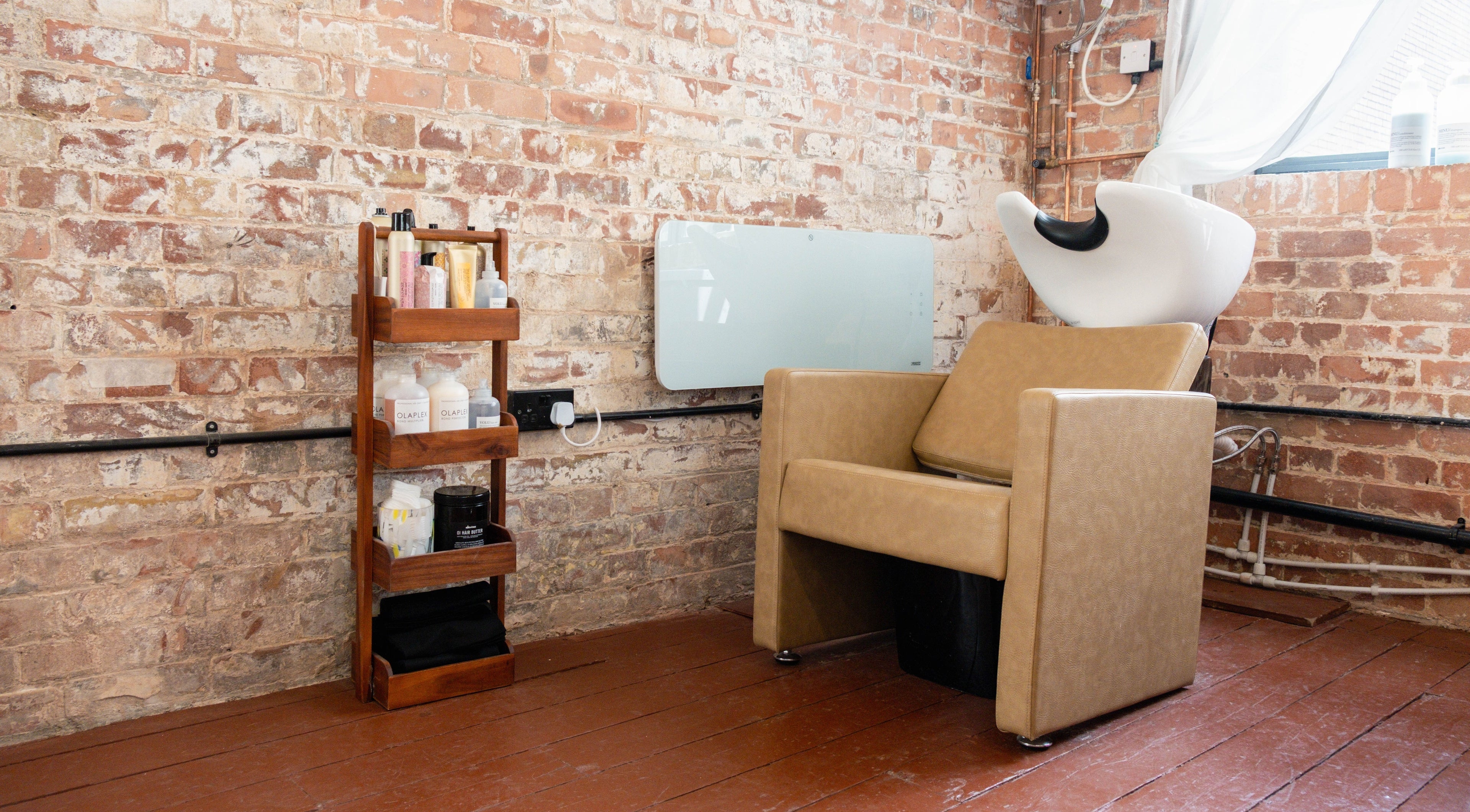 Cozy salon corner at Fluff.Hackney, London, England with a shampoo chair and product shelf against brick wall.