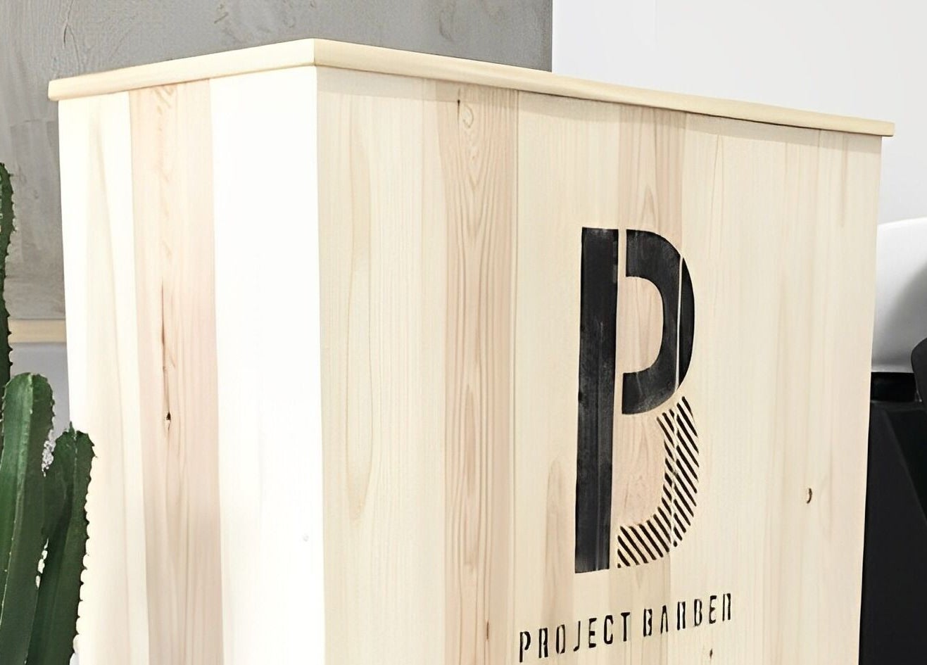 Elegant wood reception desk at Project Barber, London, England, GB with a stylish chair and cactus.