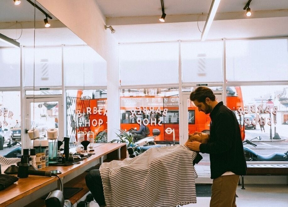 Inside Project Barber in London, England, GB, a barber prepares a client for a haircut in a stylish, bright setting.