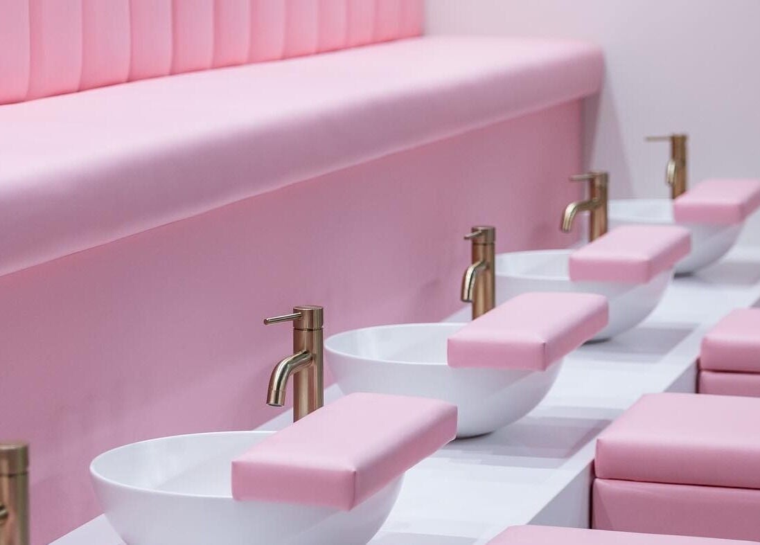 Pink nail spa seating at Leon Beauty in London, GB, featuring plush cushions and modern faucets.