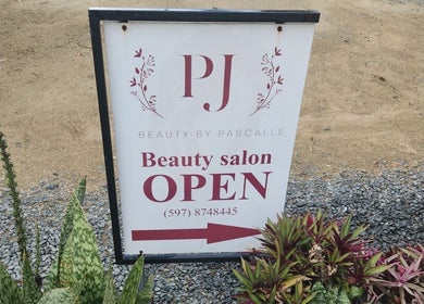 Beauty by Pascalle salon sign in Paramaribo, SR, displays 'Open' with vibrant plants around.
