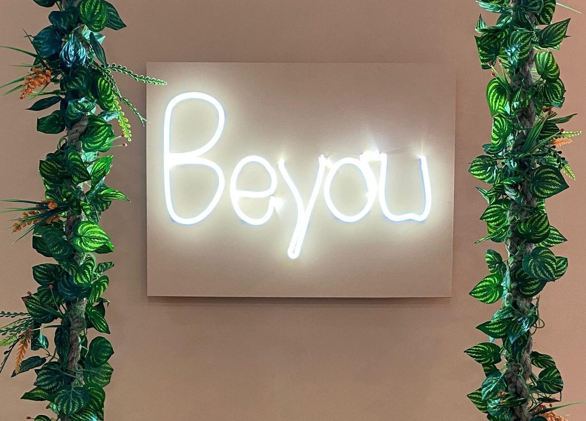 Sinal luminoso 'BeYou' em Be More You, Linda-a-Velha, Lisboa, PT, destacando decoração verde exuberante.