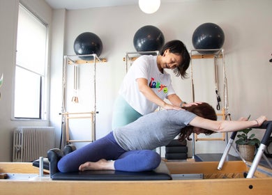 Instructor assists a client with Pilates stretching at Tomoko Pilates NYC, New York, New York, US studio.