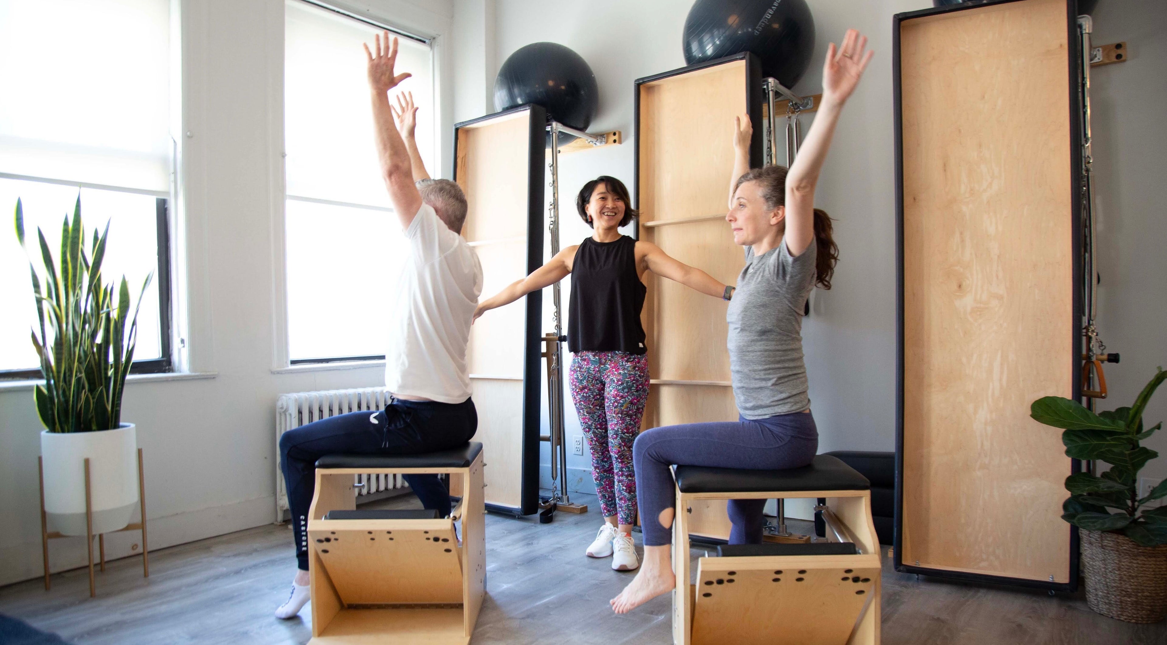 Group Pilates session at Tomoko Pilates NYC, New York, US. Bright studio with wooden equipment and plants.