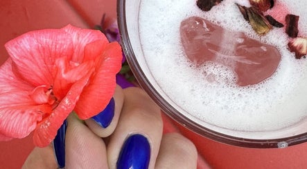 Vibrant blue nails holding floral drink at BeautyNailBar Beograd, RS, highlighting elegance and style.