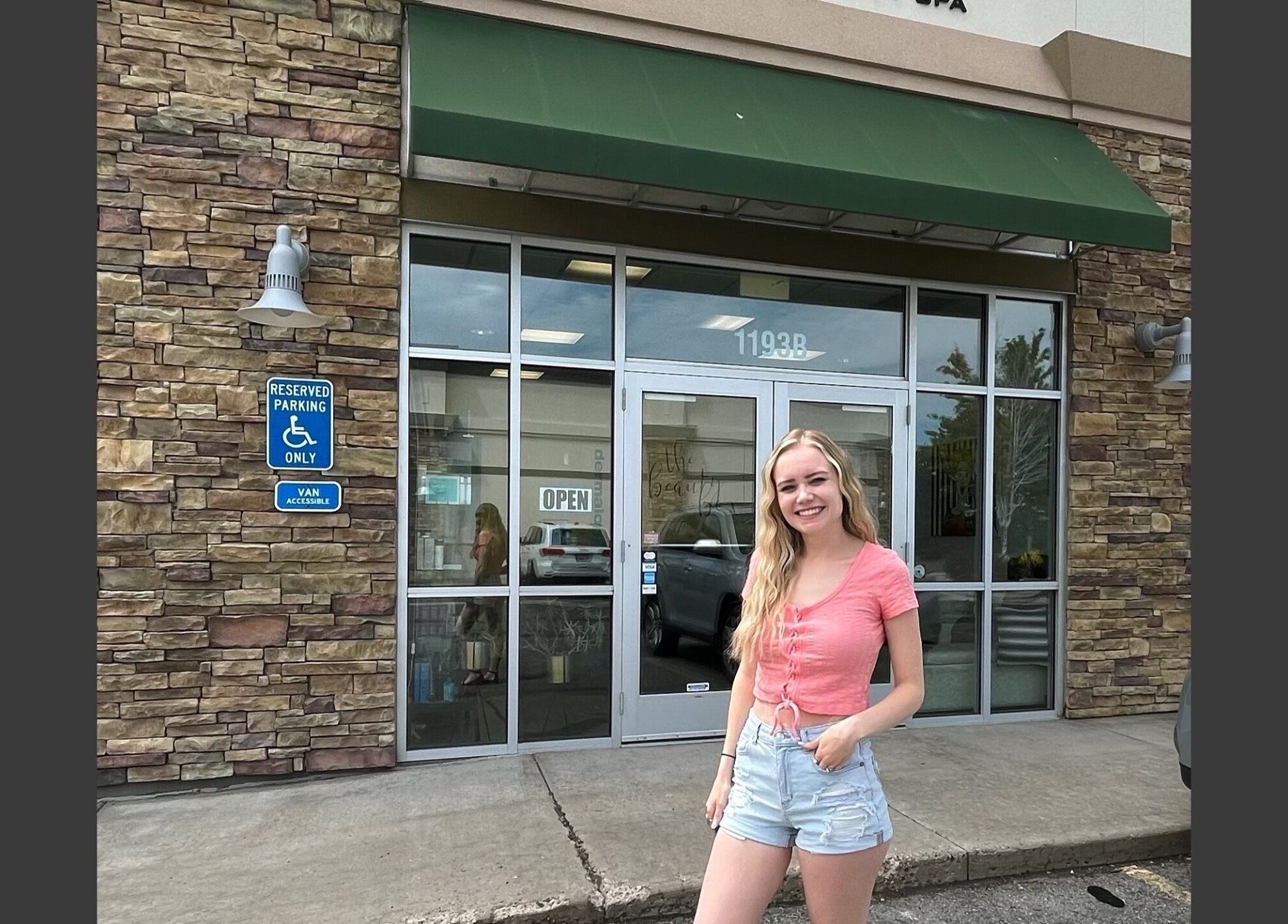 Smiling woman outside The Beauty Box entrance in Tooele, Utah, US, showcasing a welcoming atmosphere.