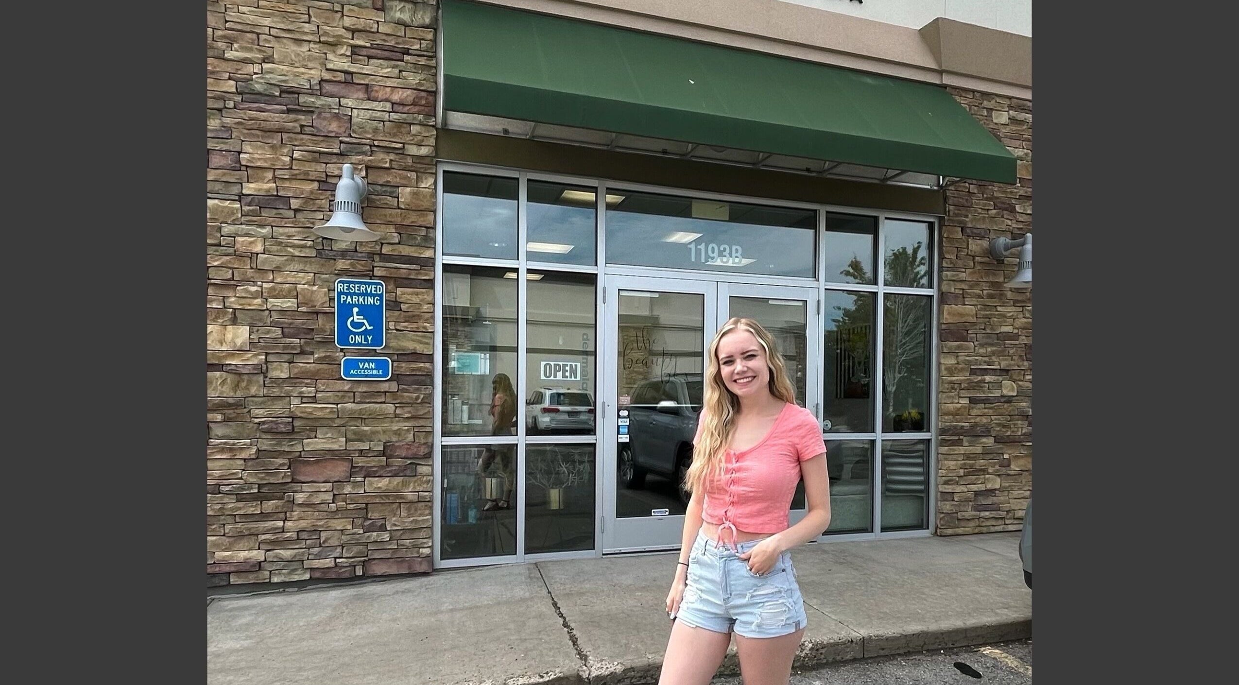 Smiling woman outside The Beauty Box entrance in Tooele, Utah, US, showcasing a welcoming atmosphere.