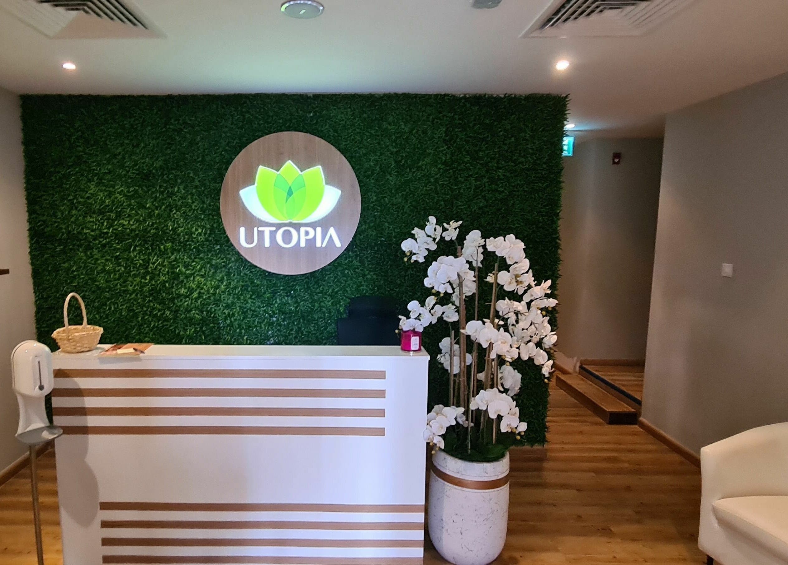 Reception area of Utopia Spa in Dubai, Dubai, AE with a green wall, desk, and white orchids.