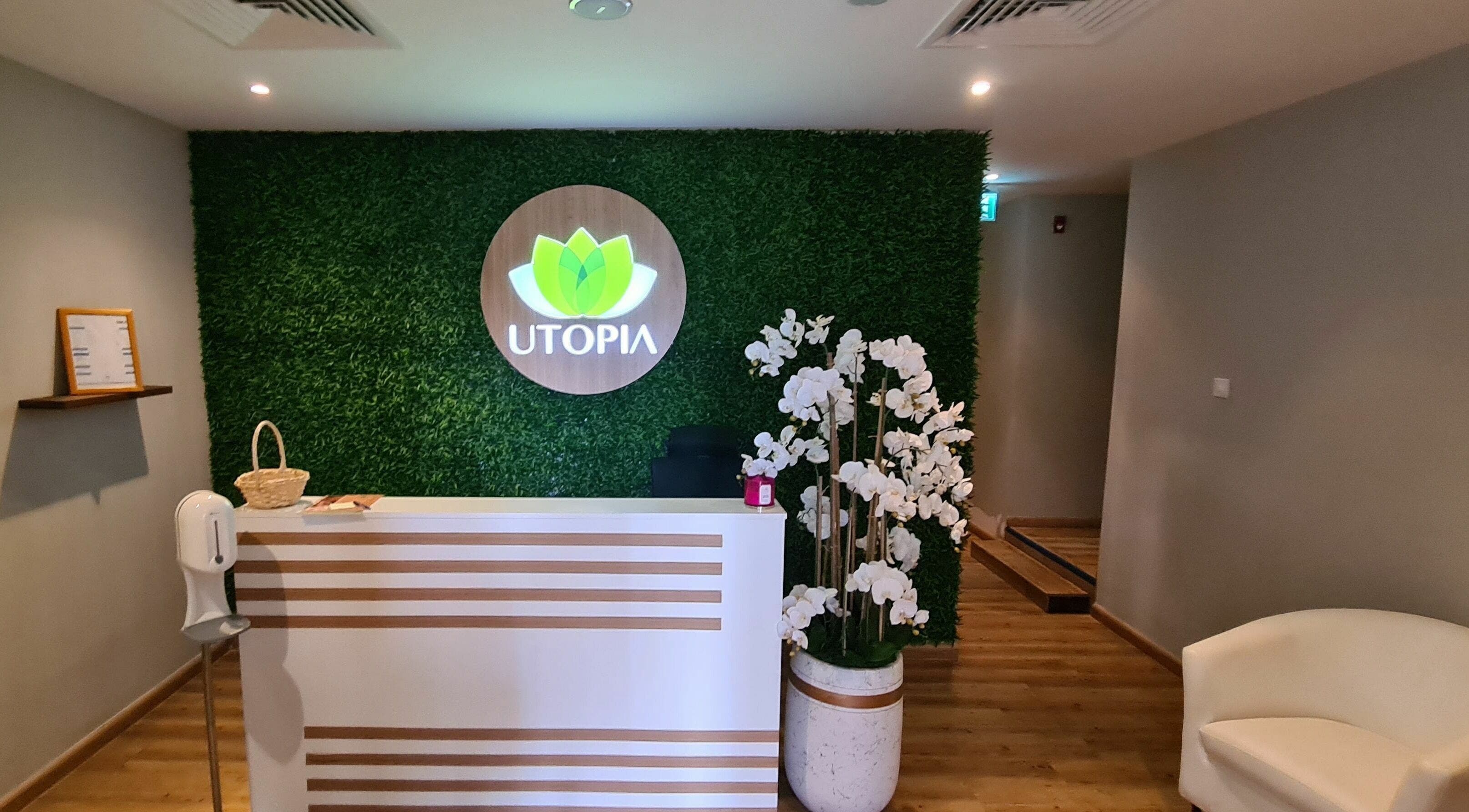 Reception area of Utopia Spa in Dubai, Dubai, AE with a green wall, desk, and white orchids.