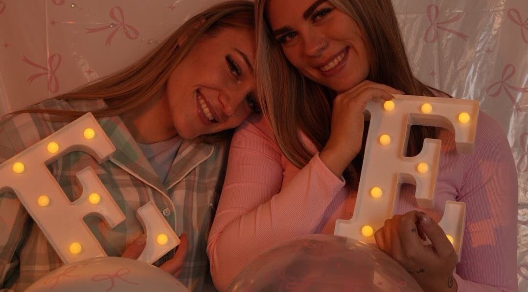 Two smiling women holding lit letters at Evil Eyes Beauty Studio, Roodepoort, Gauteng, ZA.