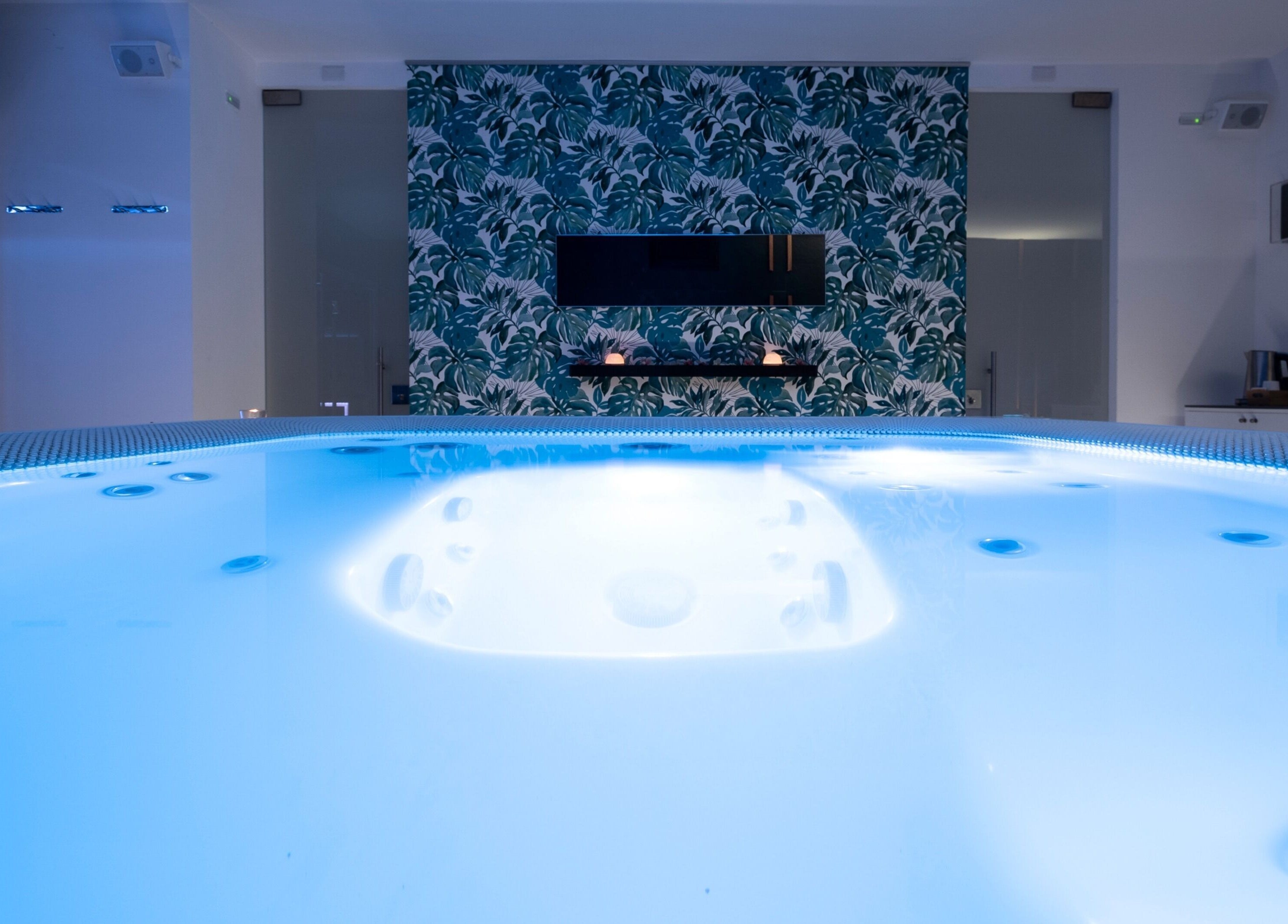 Jacuzzi blu illuminata presso Alkamuri Posh Hotel and Spa, Alcamo, Sicilia, IT, con elegante carta da parati tropicale.