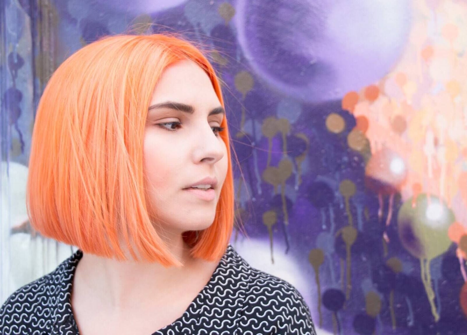Model with orange bob hairstyle at Paint London with vibrant mural backdrop, London, England, GB.