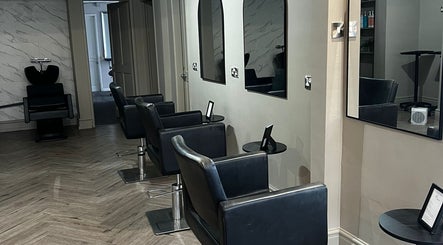 Modern salon seating area at Lucia Hair, Lostock Hall, England, GB, featuring sleek black styling chairs.