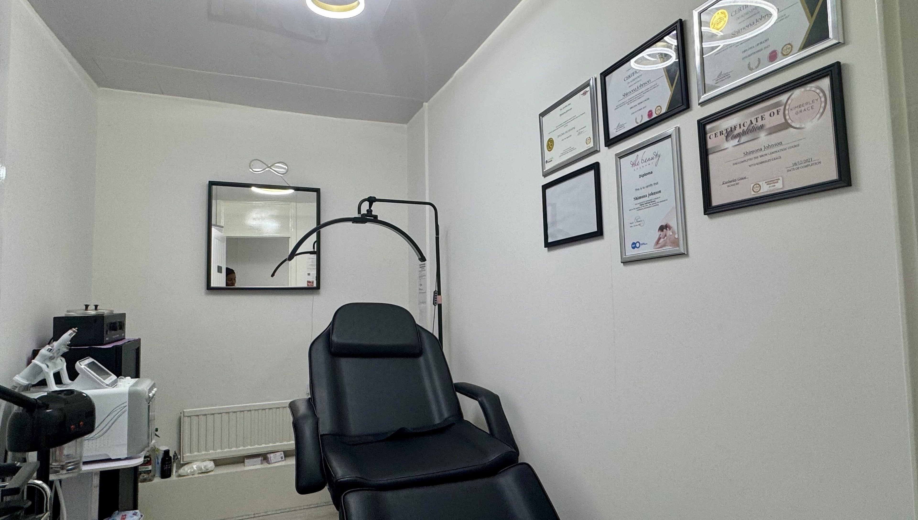 Modern treatment room at Infinite Browtential, Birmingham, England, GB with sleek equipment and certification displays.