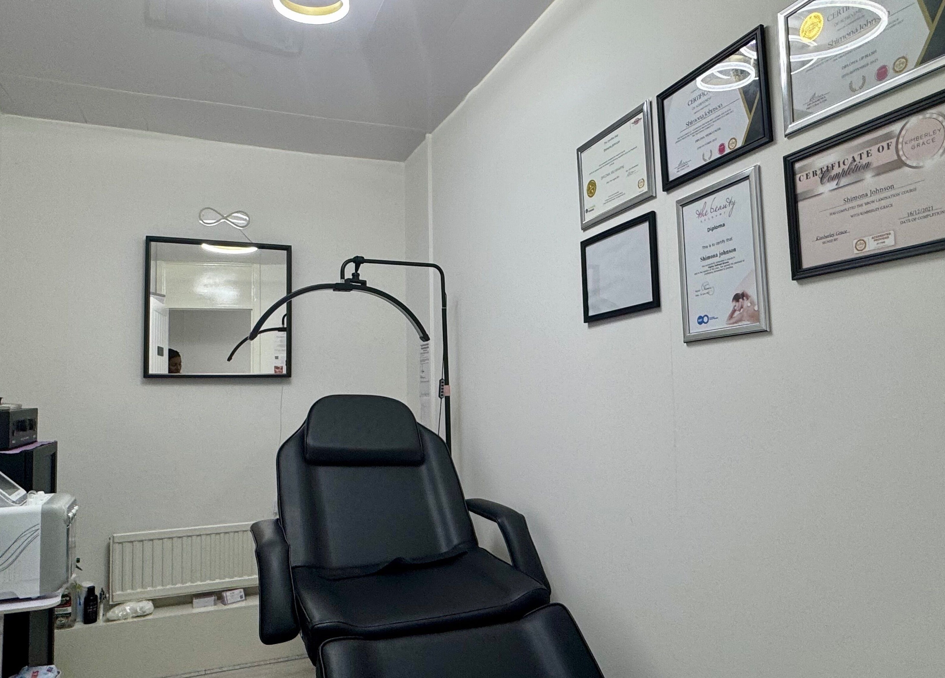 Modern treatment room at Infinite Browtential, Birmingham, England, GB with sleek equipment and certification displays.