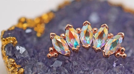 Vaughn Body Arts showcases opulent iridescent gems on a textured purple background in Monterey, California, US.
