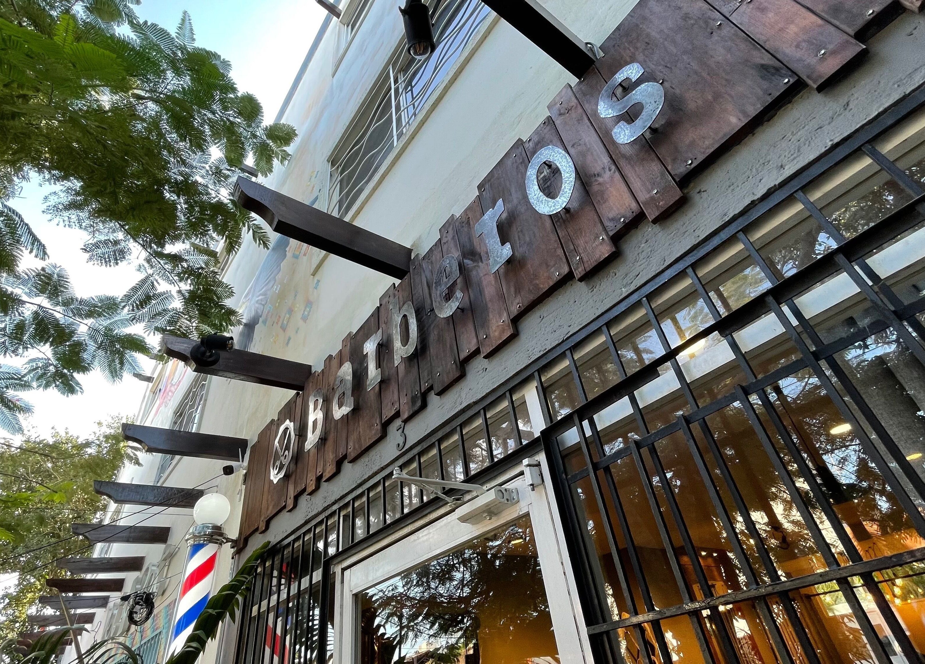 Entrada de Barberos Tulum - Av. Kukulkán en Tulum, Quintana Roo, MX, rodeada de árboles verdes.