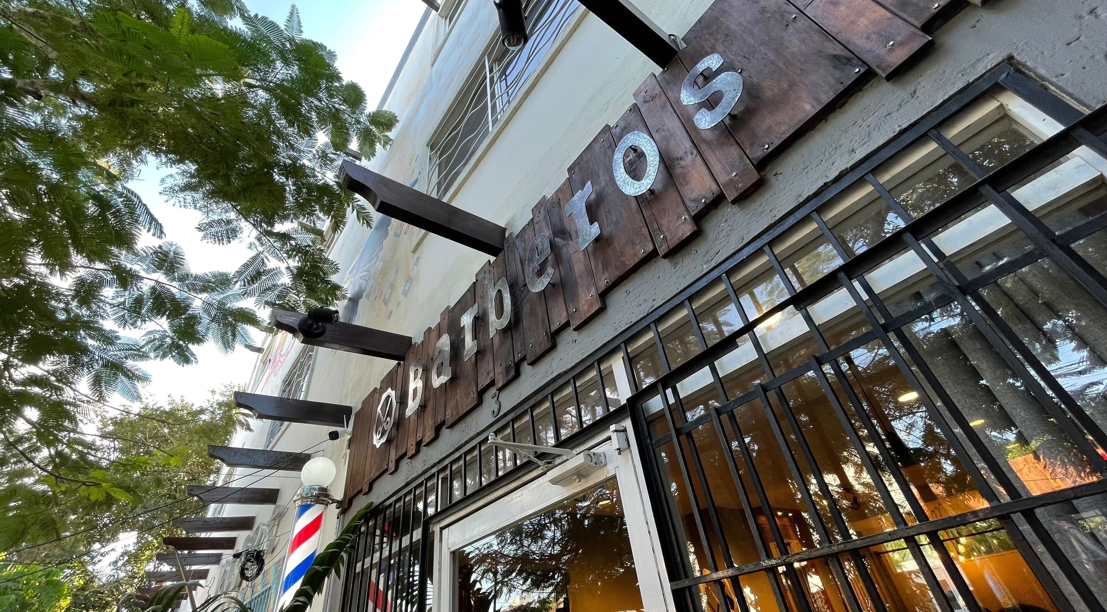 Entrada de Barberos Tulum - Av. Kukulkán en Tulum, Quintana Roo, MX, rodeada de árboles verdes.