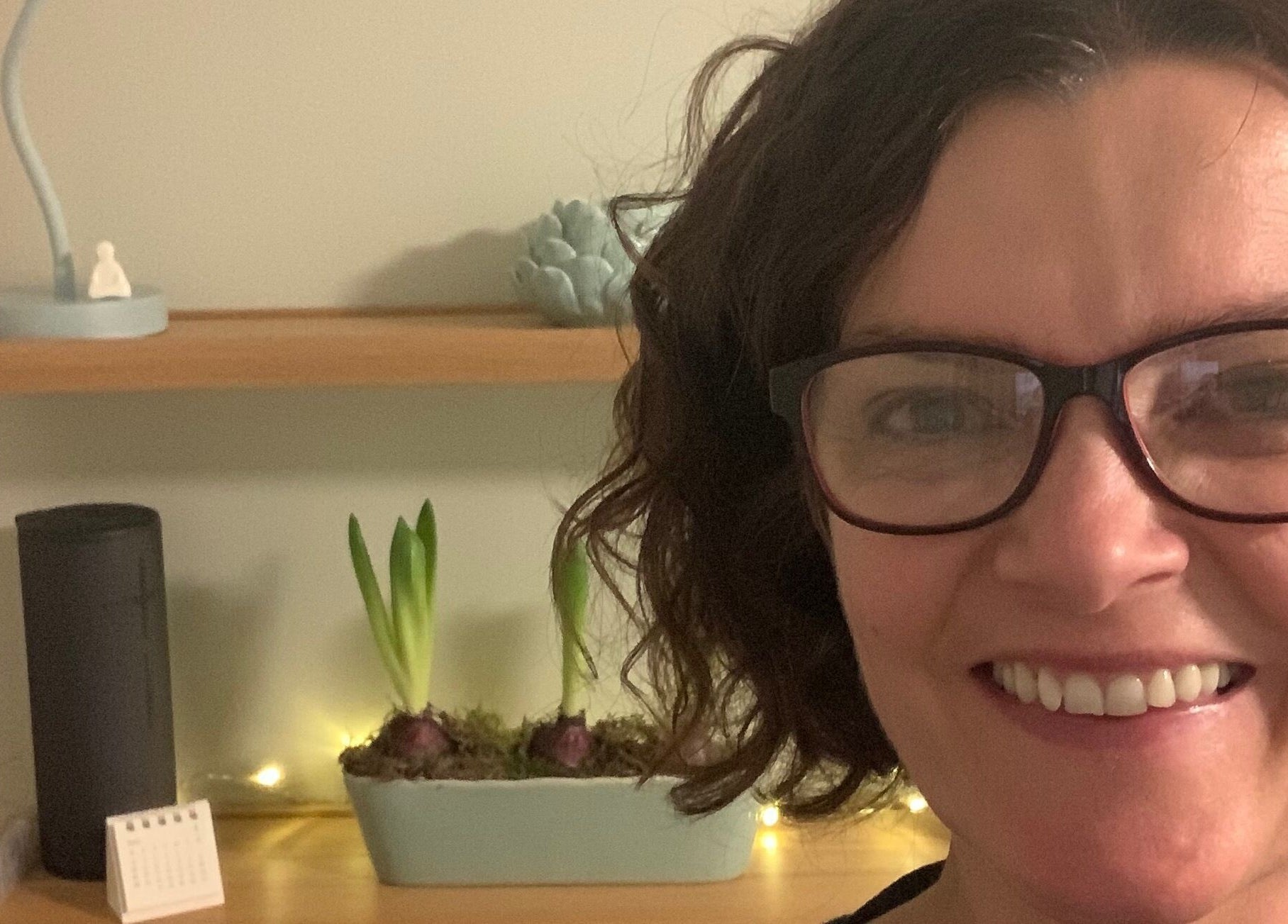 Smiling individual at Tonic Reflexology, Derby, England, GB near a shelf with plants and calming decor.