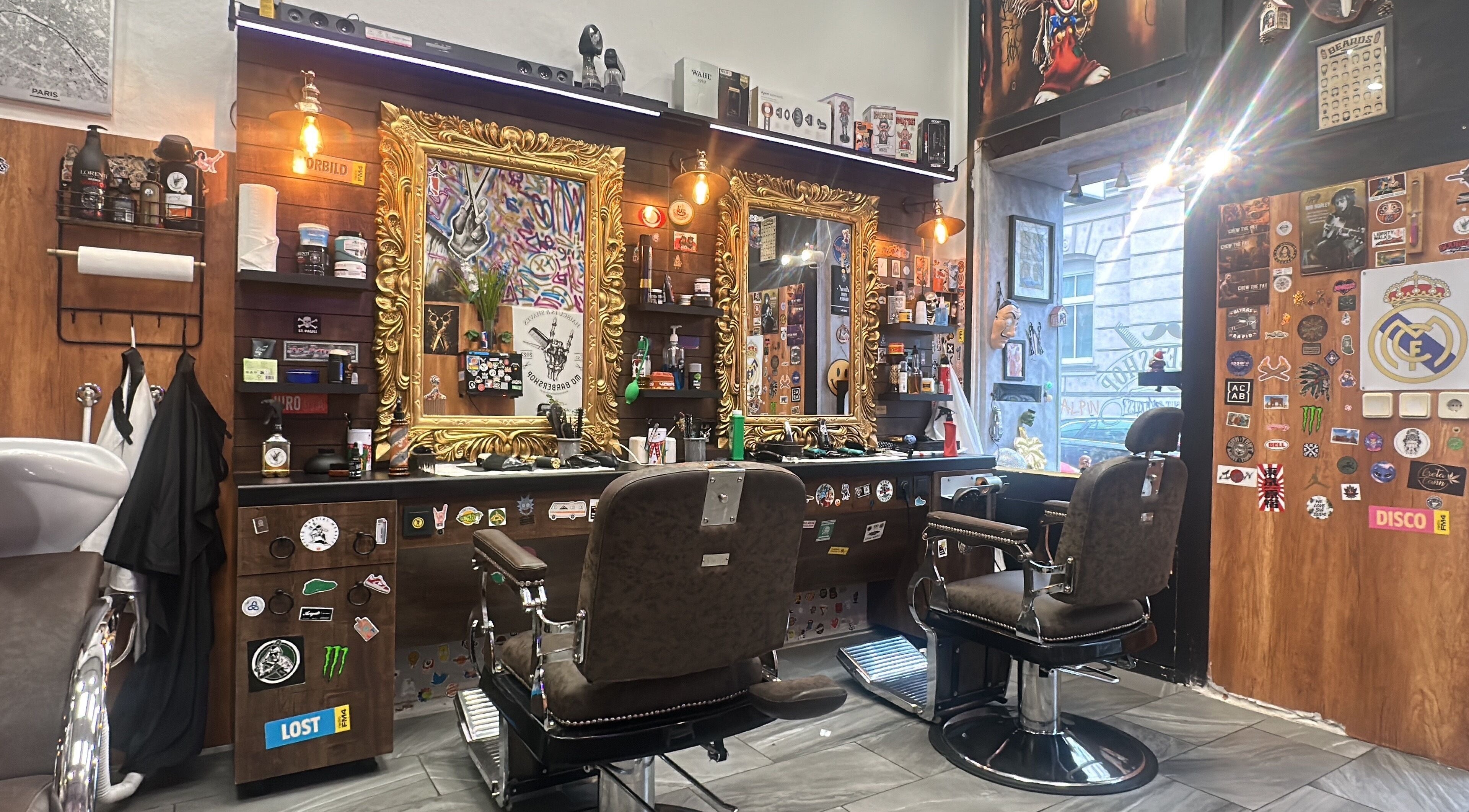 Innenansicht von Mo Barbershop in Wien, Wien, AT mit goldenen Spiegeln und stilvollen Friseurstühlen.