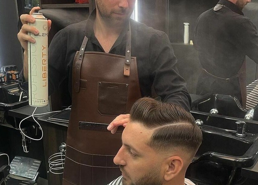 Stilist la HiStory Barbershop Camil Ressu 8, București, RO, aplicând fixativ pentru o coafură modernă.