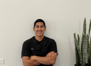 Barbero sonriente en Barbería Boss C.Colima, Tijuana, Baja California, MX junto a planta decorativa.