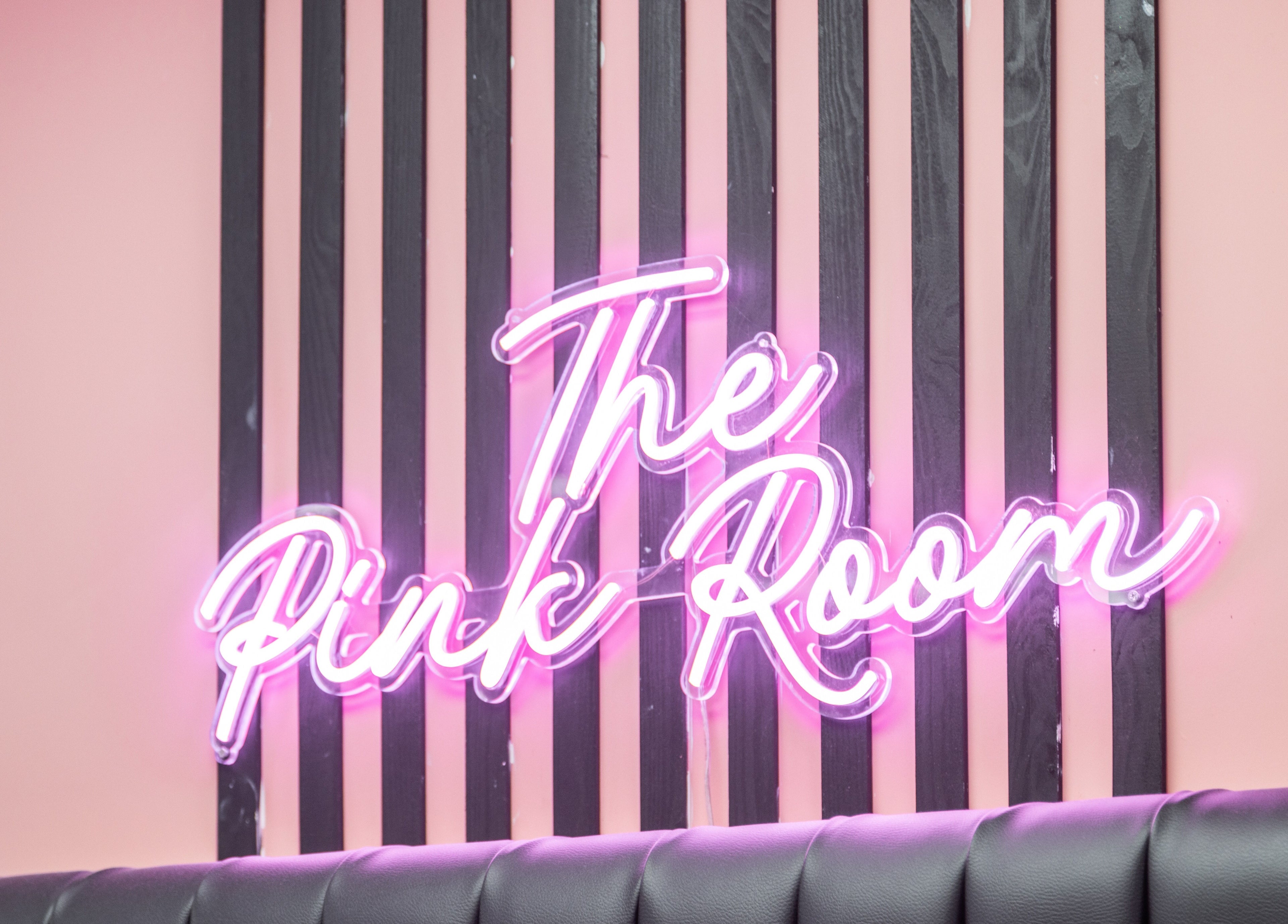 Pink neon sign of The Pink Room at Warrington, England, GB, stylishly displayed on elegant striped wall.