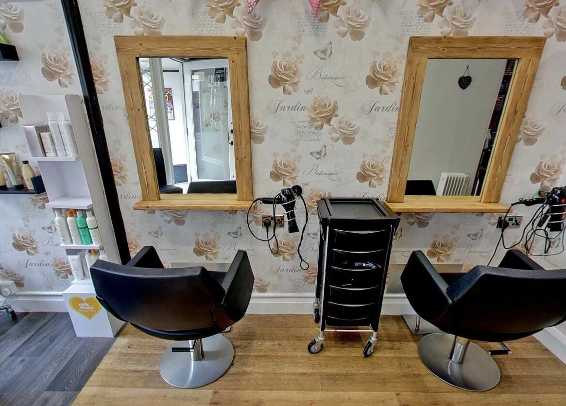 Elegant hairstyle stations at Studio 26 in Royston, England, GB with stylish chairs and rose-patterned walls.