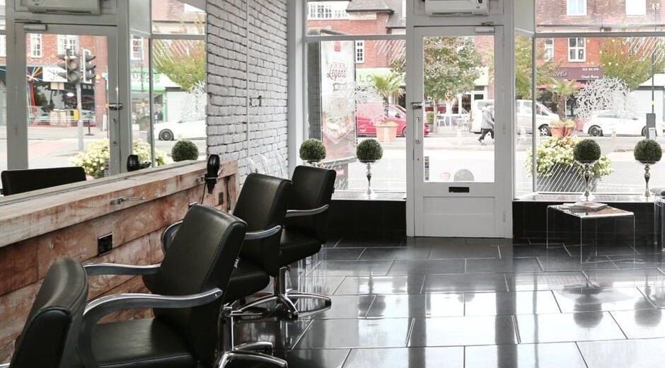 Stylish interior of Chair-Sam Slater salon, Birmingham, England, GB with modern seating and street view.