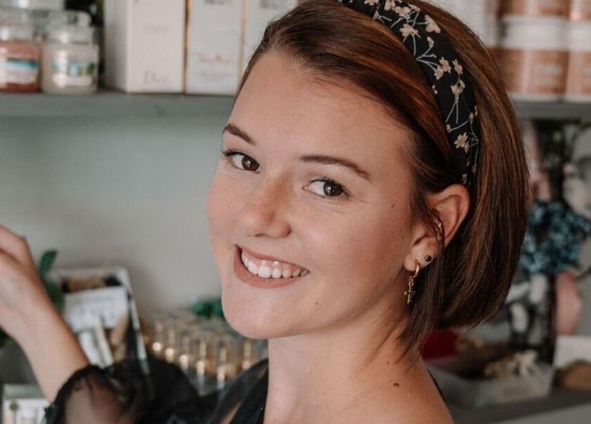 Smiling woman at Smashed Beauty in Jeffreys Bay, Eastern Cape, ZA, surrounded by beauty products on display.