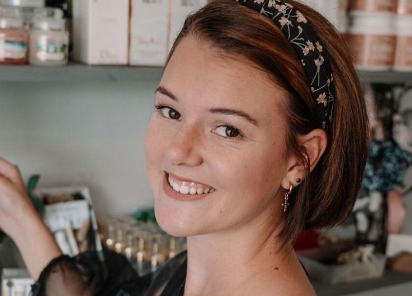 Smiling woman at Smashed Beauty in Jeffreys Bay, Eastern Cape, ZA, surrounded by beauty products on display.