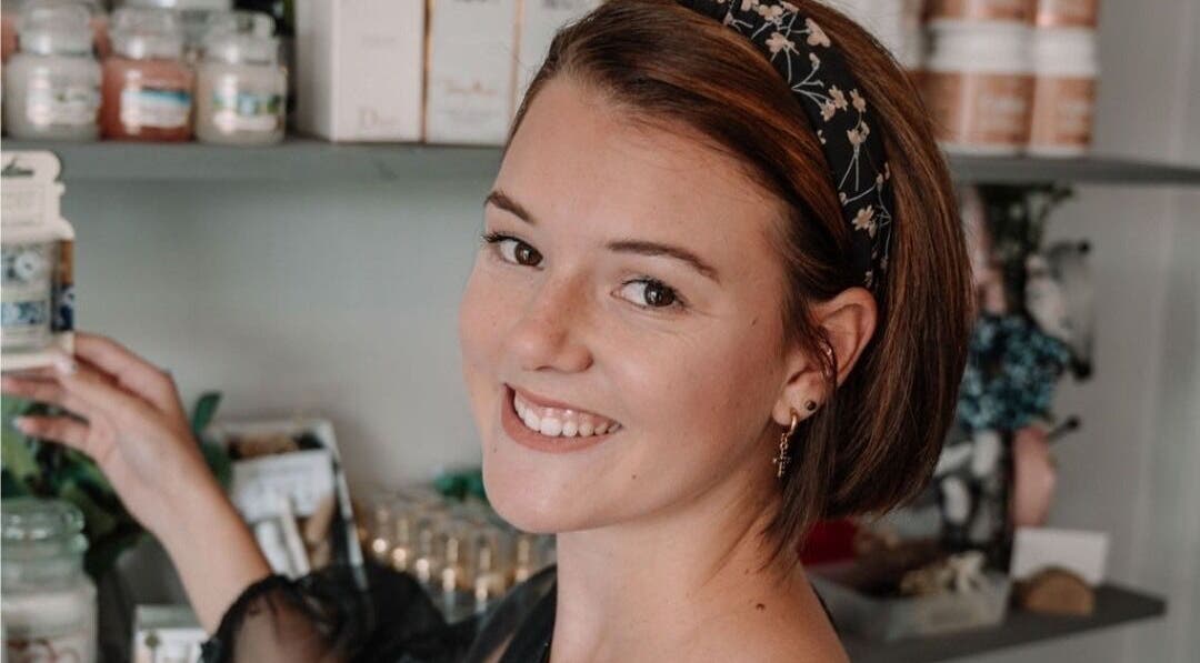 Smiling woman at Smashed Beauty in Jeffreys Bay, Eastern Cape, ZA, surrounded by beauty products on display.