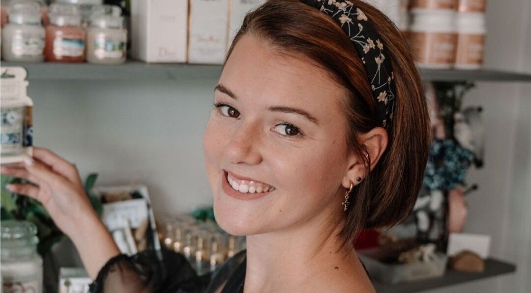 Smiling woman at Smashed Beauty in Jeffreys Bay, Eastern Cape, ZA, surrounded by beauty products on display.