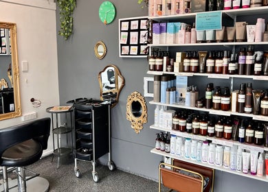 Inside Blink Hair Design, Christchurch, Canterbury, NZ, showcasing elegant styling chairs and a wall of premium hair products.