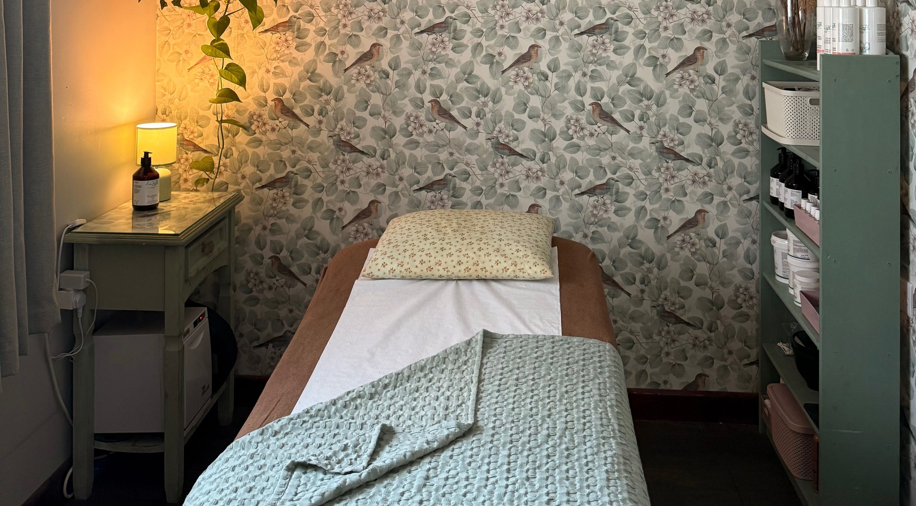 Cozy massage room at Blossom Cottage Beauty in Rugby, England, GB with floral wallpaper and ambient lighting.
