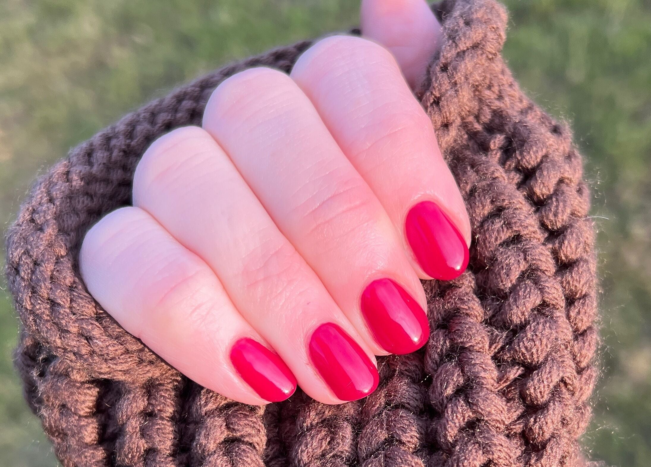 Close-up of vibrant red polished nails at By Bethany Rose, Hatfield, England, GB, wrapped in a cozy knit.