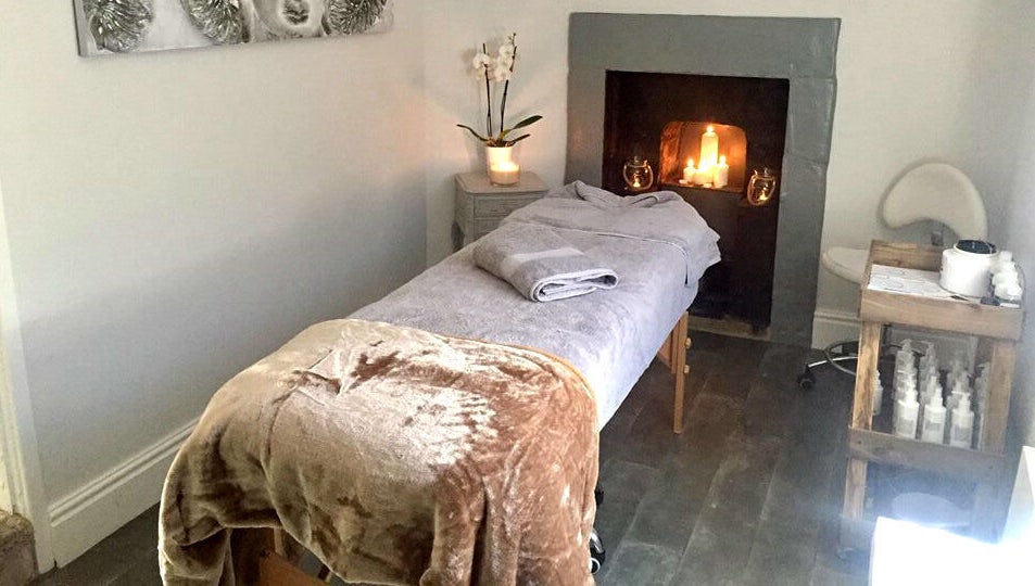 Cozy massage room at Azuri, Ripon, England, GB featuring a comfortable table and lit fireplace.