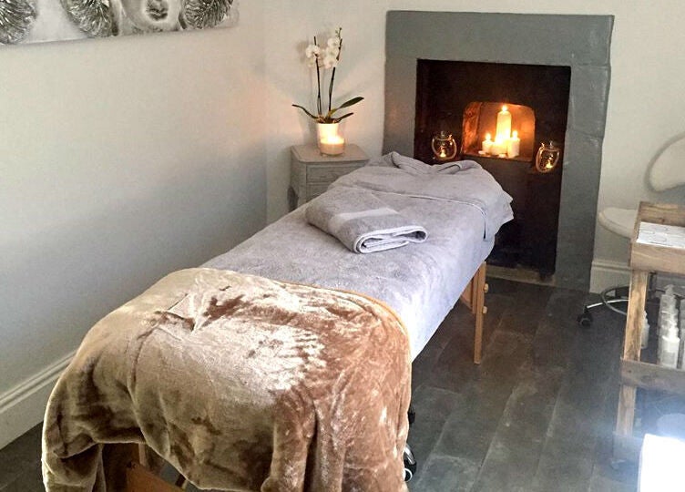 Cozy massage room at Azuri, Ripon, England, GB featuring a comfortable table and lit fireplace.