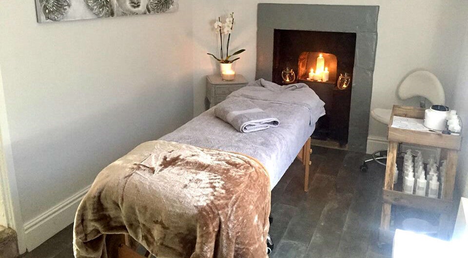 Cozy massage room at Azuri, Ripon, England, GB featuring a comfortable table and lit fireplace.