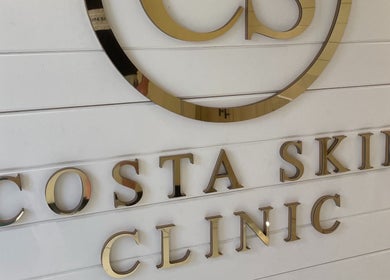Costa Skin Clinic sign in Alnwick, England, GB featuring elegant golden lettering on a white background.