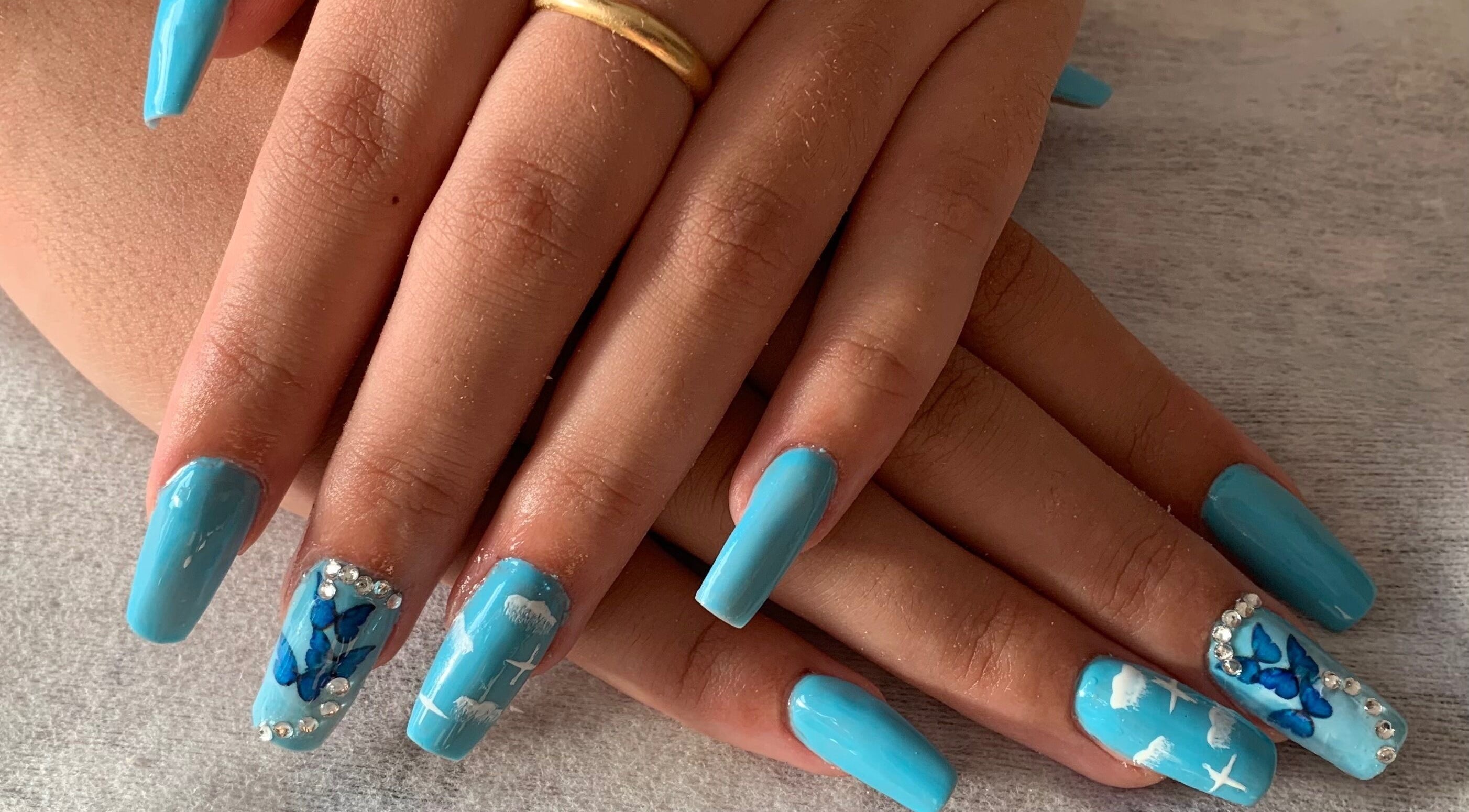 Uñas azules con diseño de mariposa y pedrería en ByBeauty, Sant Celoni, Catalunya, ES.